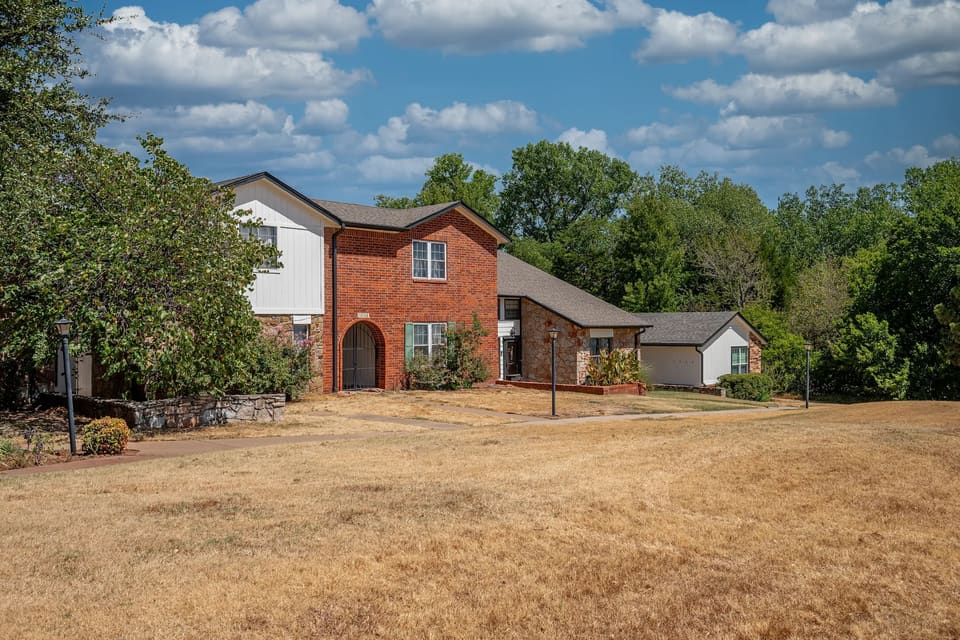 Two-story brick townhome building at The Crossing in Edmond, OK with freshly painted off-white siding and dark trim under a summer sky